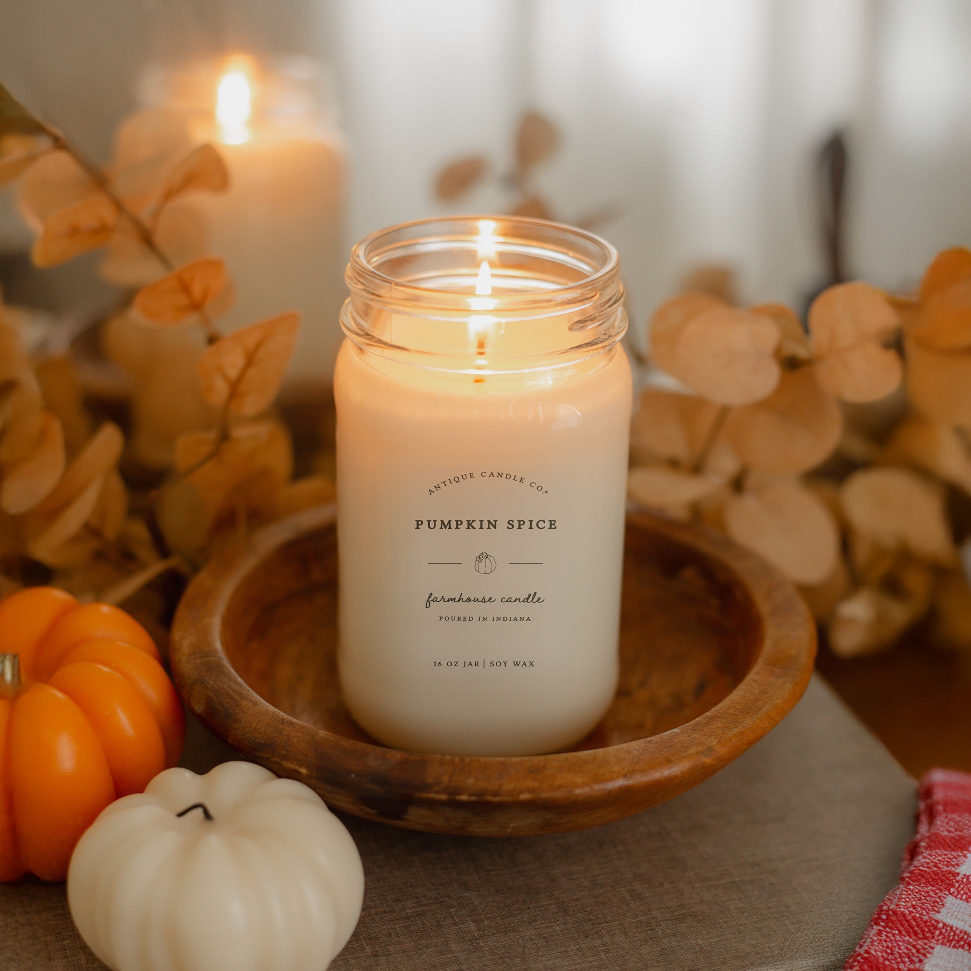 Candle labeled 'Pumpkin Spice' in a jar on a wooden tray with pumpkins and leaves.