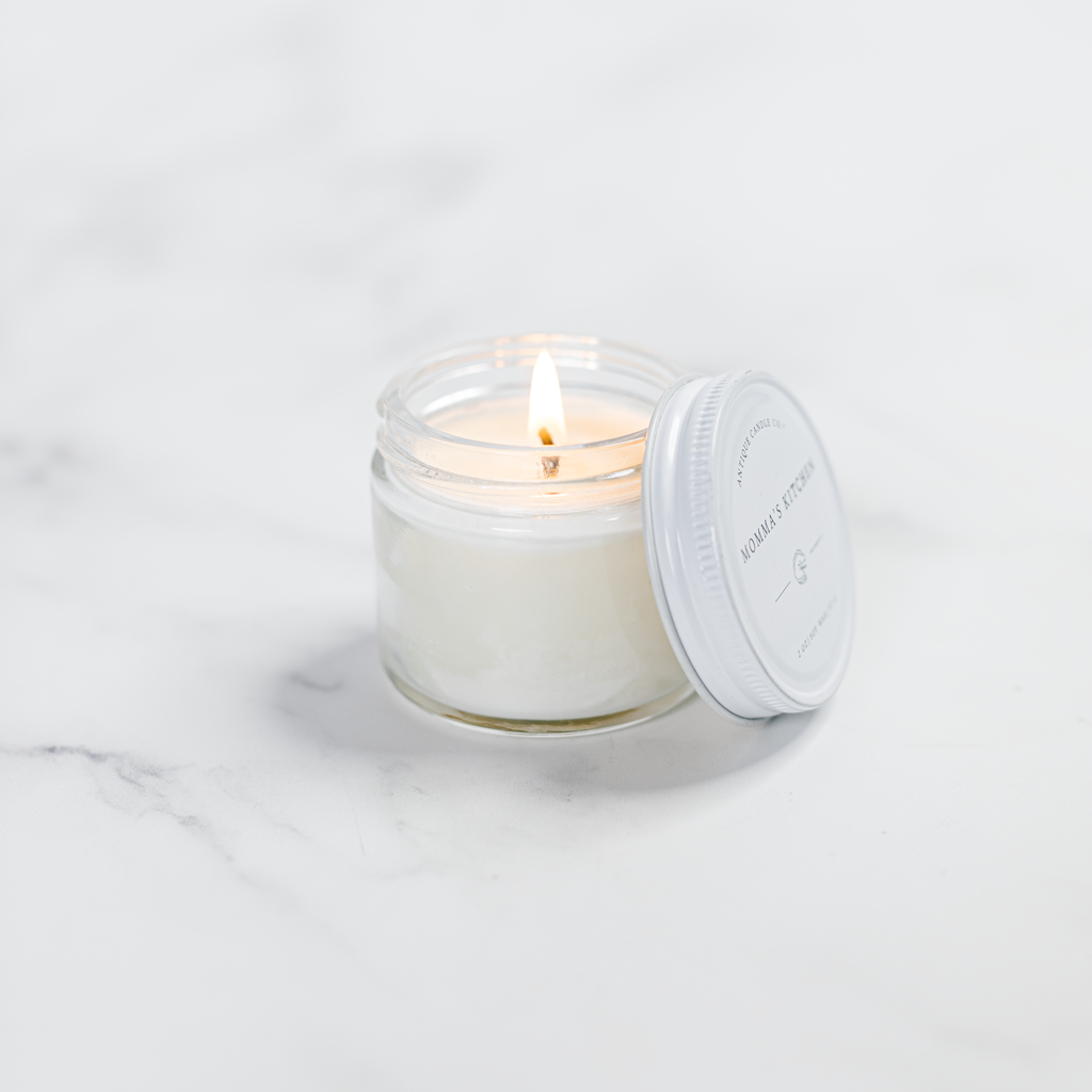 Lit candle in a glass jar with a white lid on a light gray background